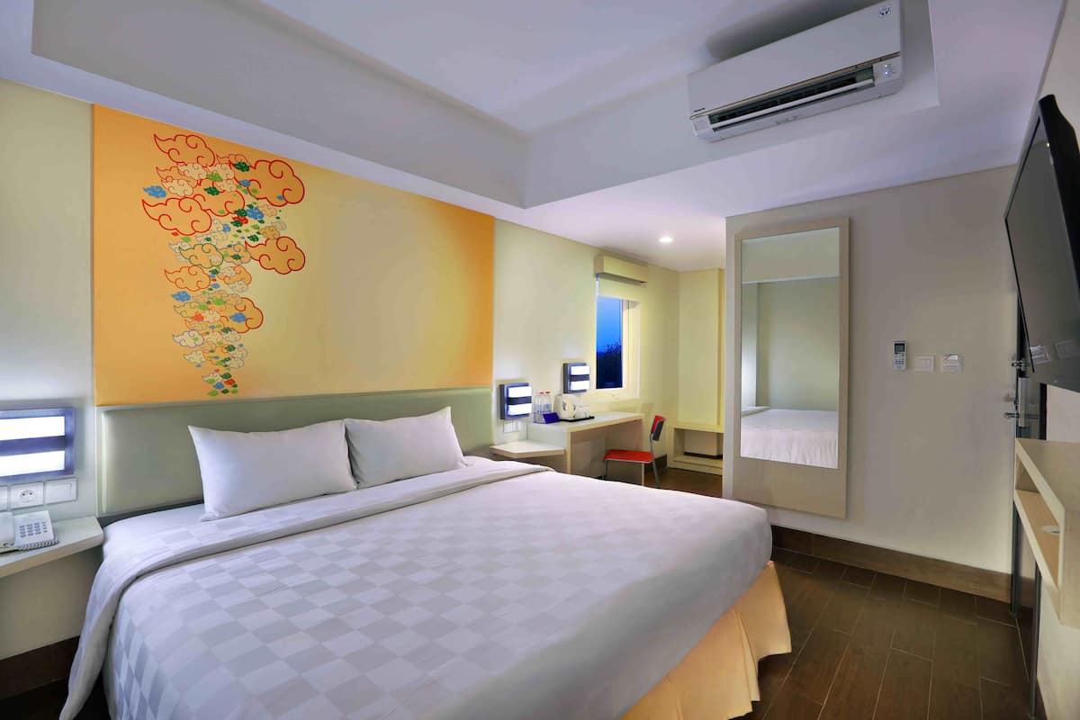 Ein Hotelzimmer mit einem großen Bett, einem Schreibtisch, einem Sessel, einem Fernseher und einer Klimaanlage.