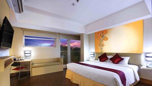 A hotel room with a large bed, a desk with a chair, a television, and a window with a cityscape view.