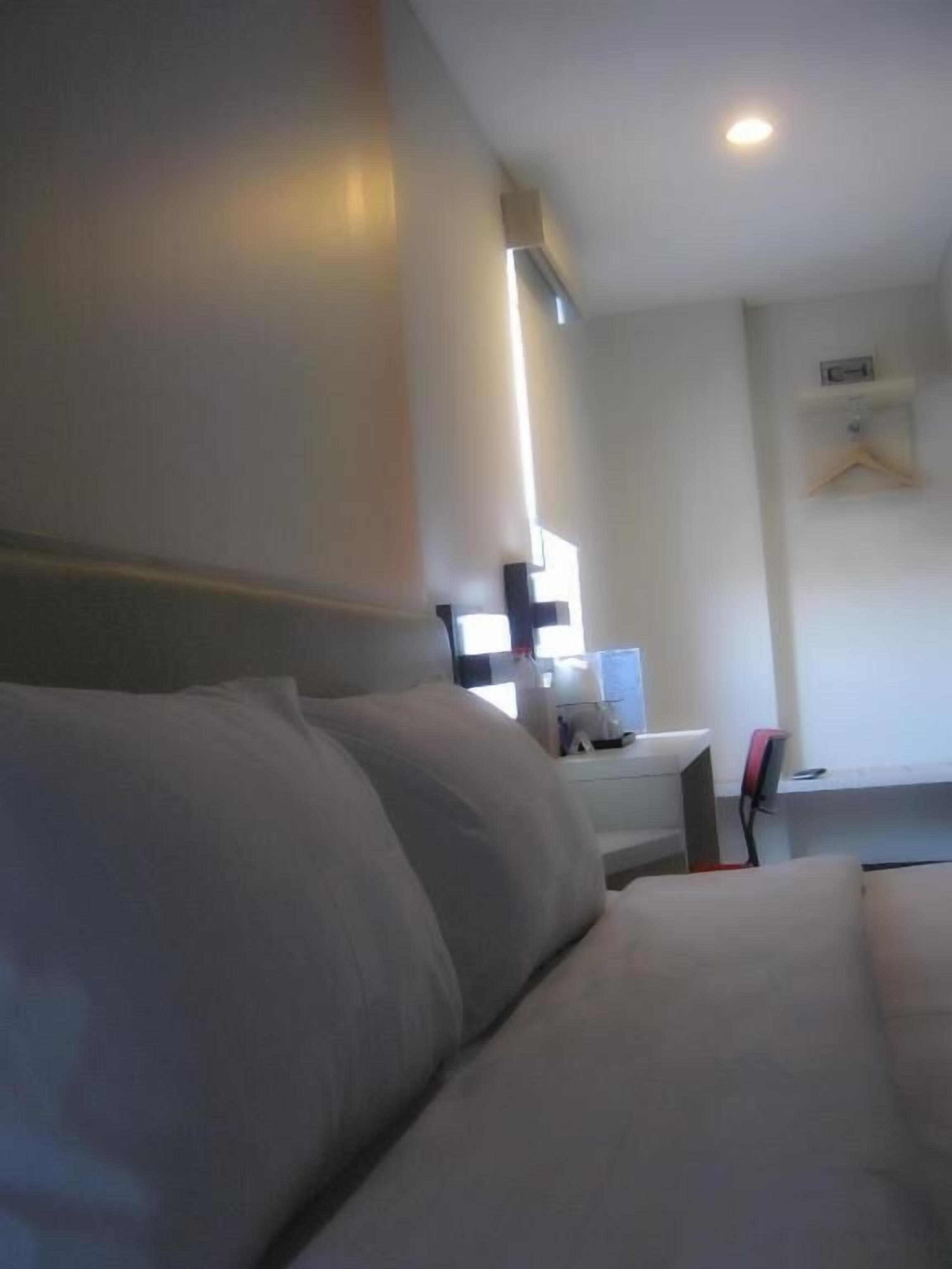 A hotel room with a bed, a desk with a chair, and a small table with a lamp.