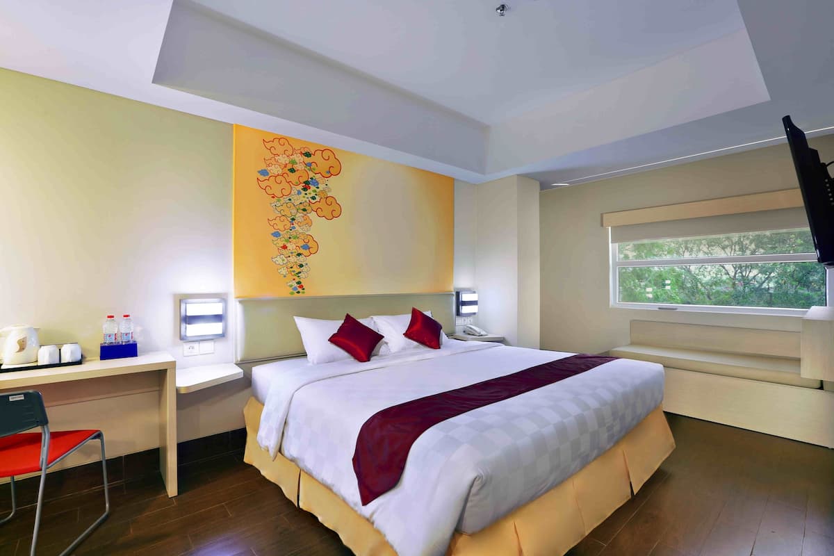 Ein Hotelzimmer mit einem großen Bett, einem Schreibtisch mit Stuhl, einem Fenster mit Aussicht und einer Wand mit floralem Wandbild.