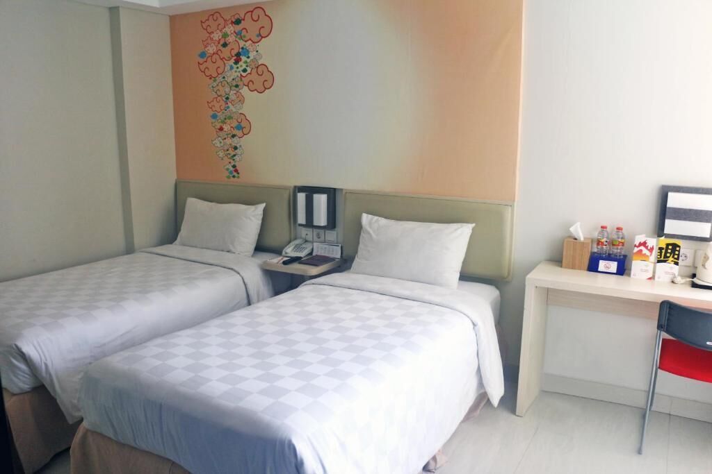 A hotel room with two beds, a desk, a chair, and a wall decoration.