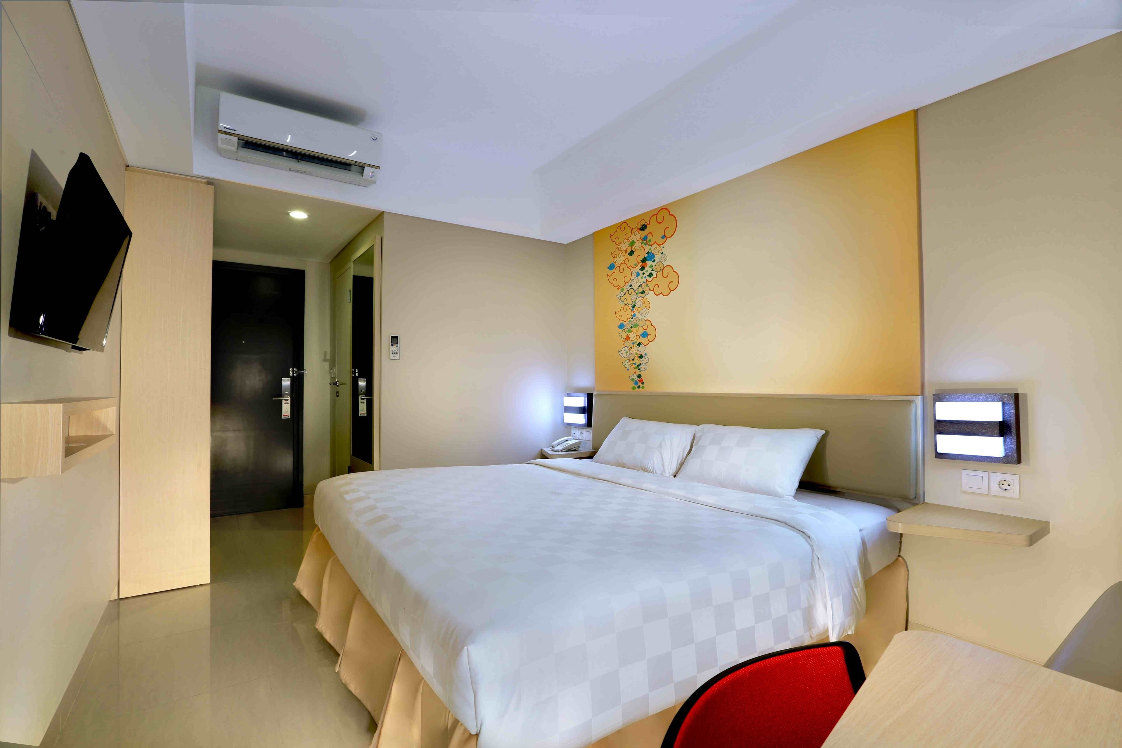 Una camera d'albergo moderna con un letto grande, una TV a schermo piatto montata a parete, un condizionatore d'aria e un elemento decorativo al muro.