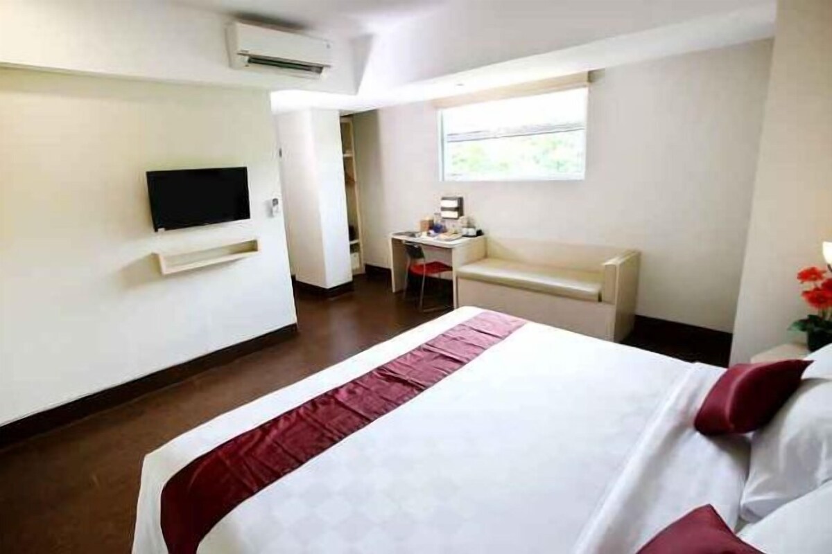 A hotel room with a bed, a desk, a chair, a television, and a window.