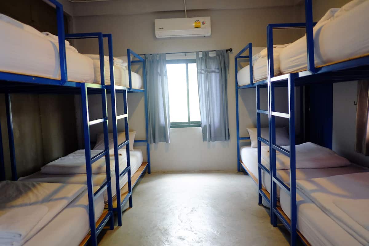 A dormitory room with bunk beds, a window with curtains, and an air conditioning unit.