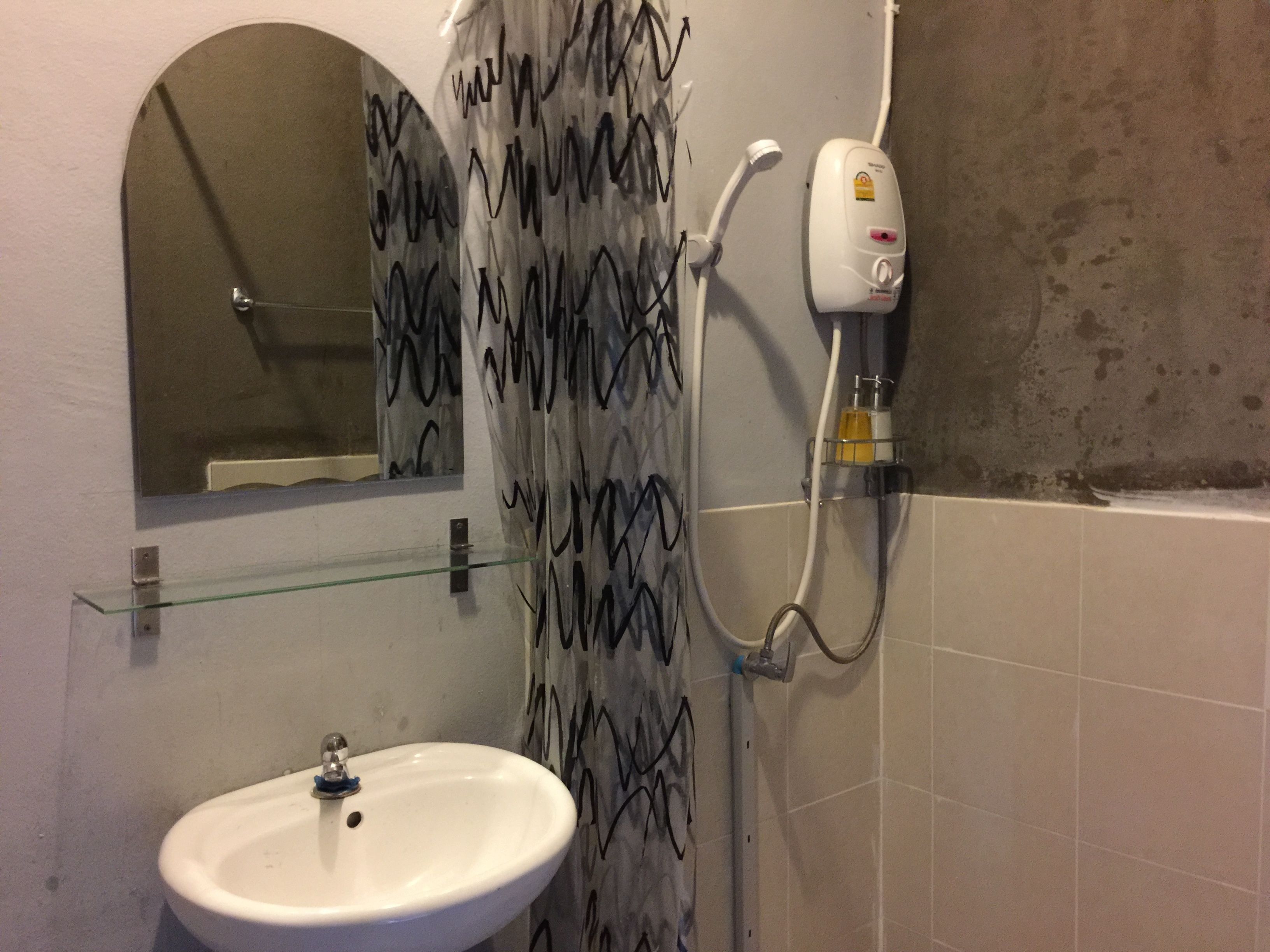 Un baño con un lavabo blanco, un estante de vidrio, una ducha con cortina estampada, un cabezal de ducha manual y un dispensador de jabón.