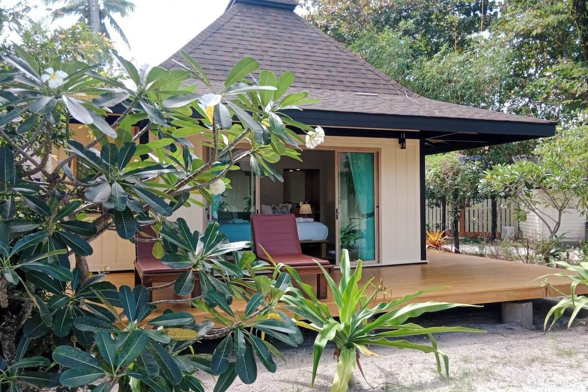 Een bungalow met een overdekt terras, een zwembad en weelderige begroeiing.