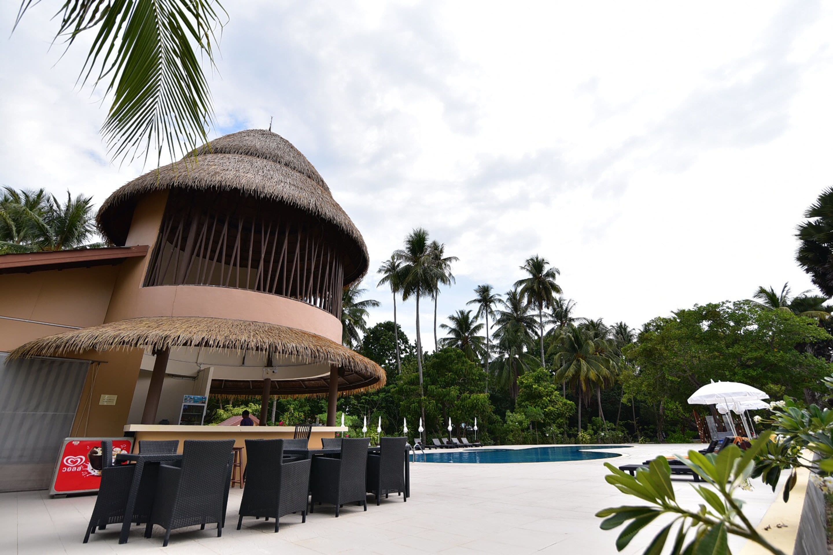A resort with a thatched-roof structure, outdoor seating, and a pool area surrounded by palm trees.