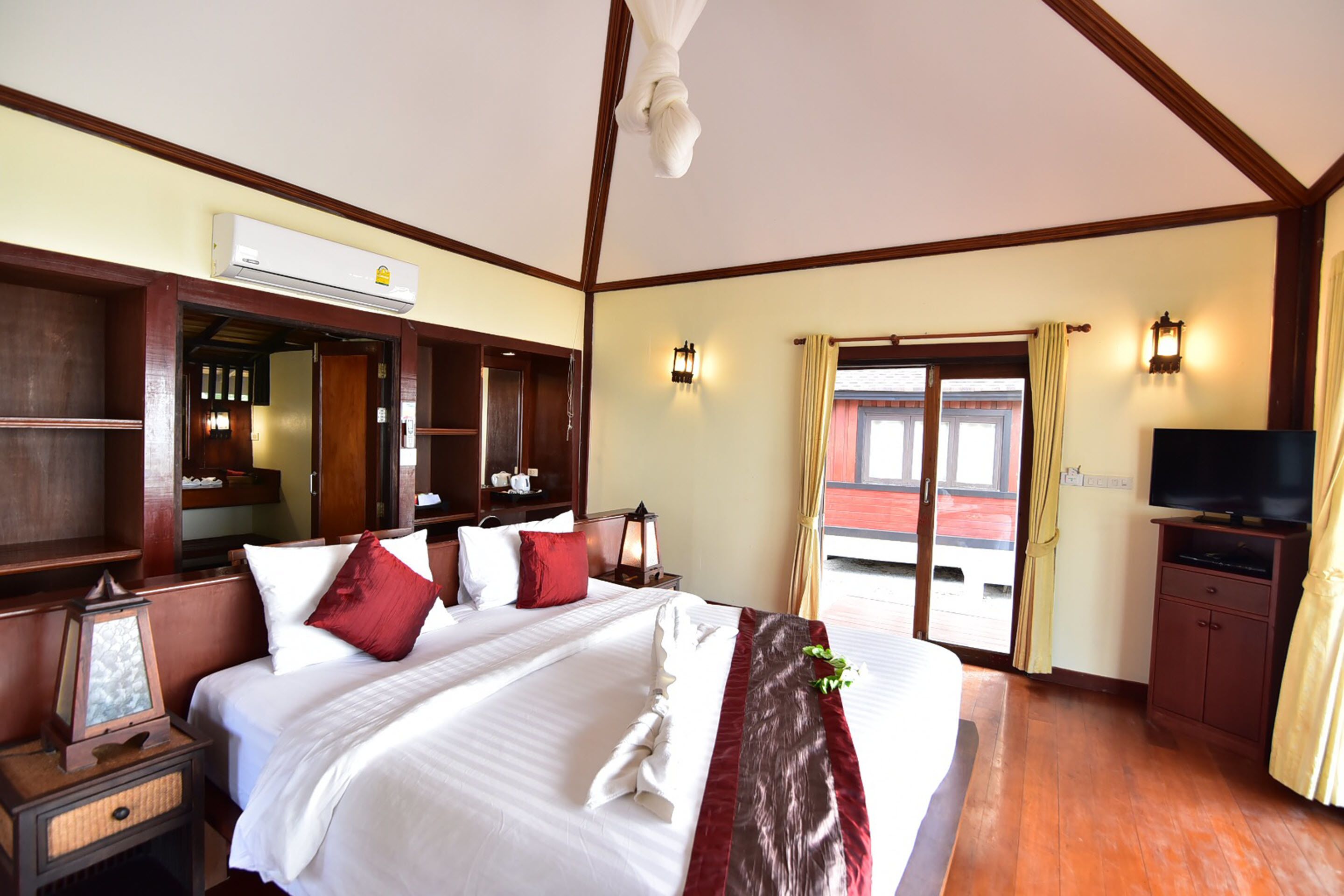 Habitación de hotel con una cama grande, cabecero de madera, un equipo de aire acondicionado, un televisor y vistas al exterior.