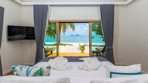 Een hotelkamer met een bed, een flatscreen televisie en uitzicht op het strand.