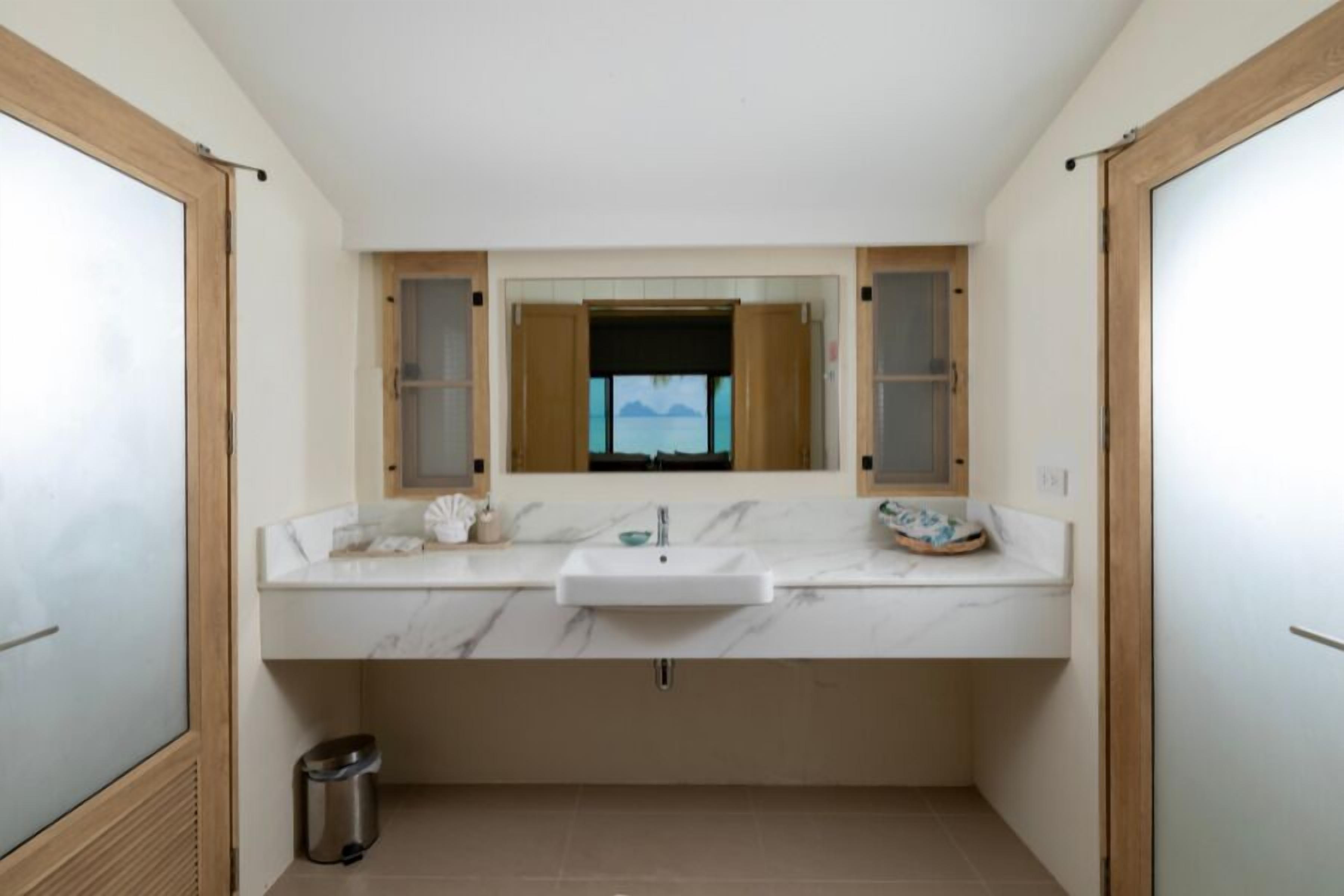 A bathroom with a white marble sink, wooden cabinets, and a window with a view.