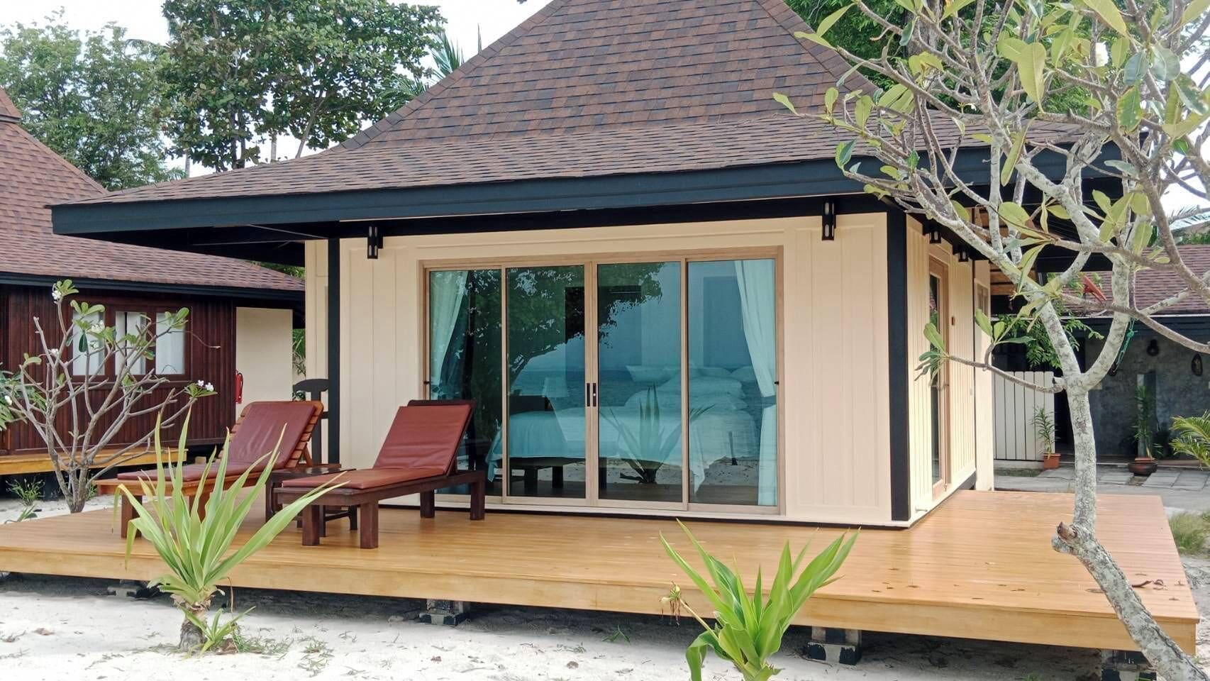 A modern villa with a large sliding glass door, a wooden deck, and two red lounge chairs.