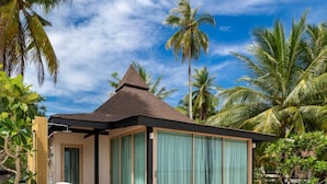 Een modern strandhuis met een gebogen houten terras, grote schuifdeuren en een kegelvormig dak.
