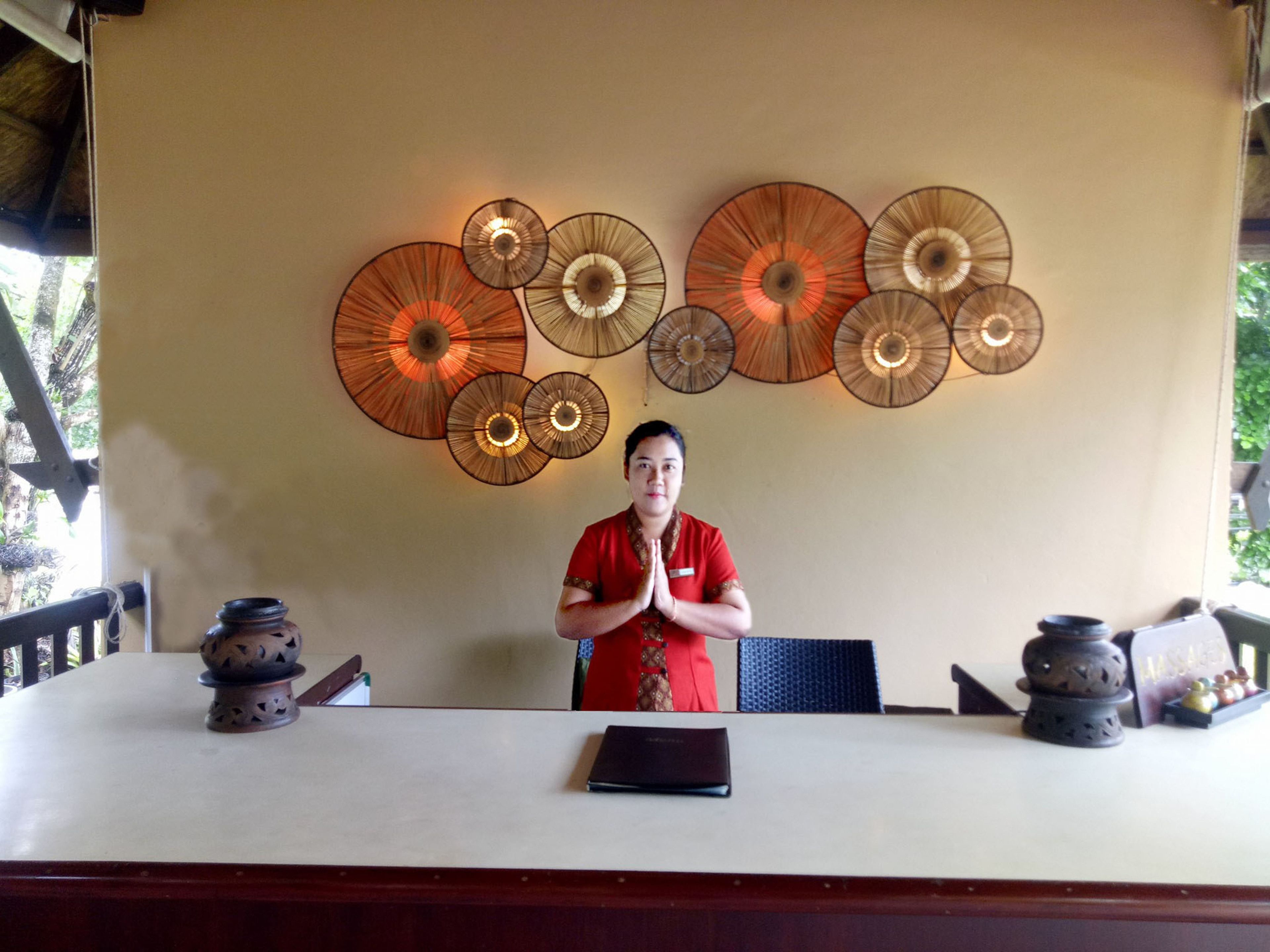 A person seated at a table with a laptop, surrounded by decorative wall art and a traditional incense burner.