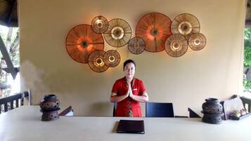 A person seated at a table with a laptop, surrounded by decorative wall art and a traditional incense burner.
