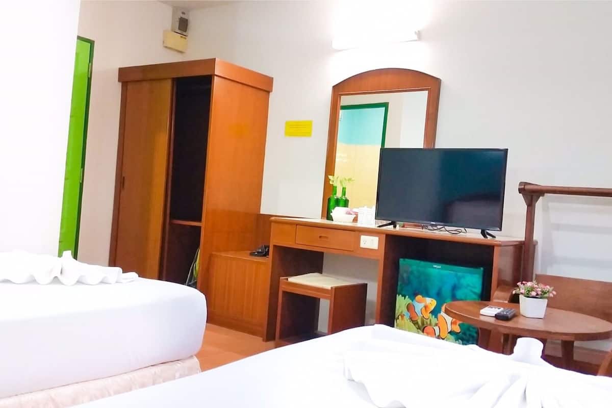 A hotel room with a bed, a desk with a computer, a television, and a small table with a plant.