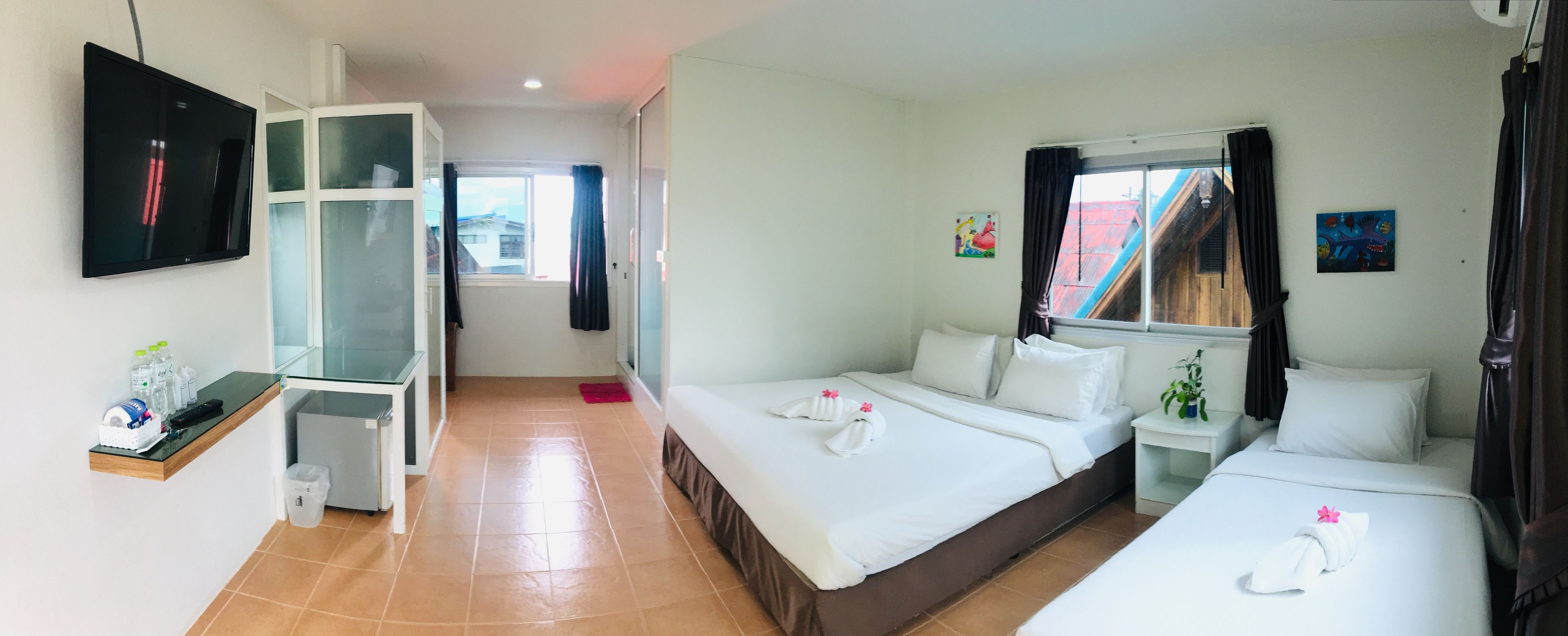 A hotel room with two beds, a TV, a small table with toiletries, and a window with curtains.
