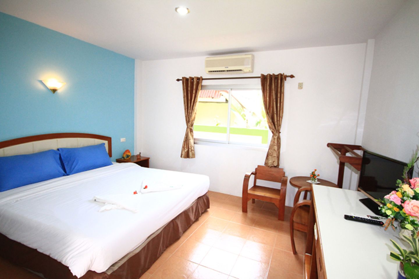 A hotel room with a bed, a desk, a chair, a TV, and a window with curtains.