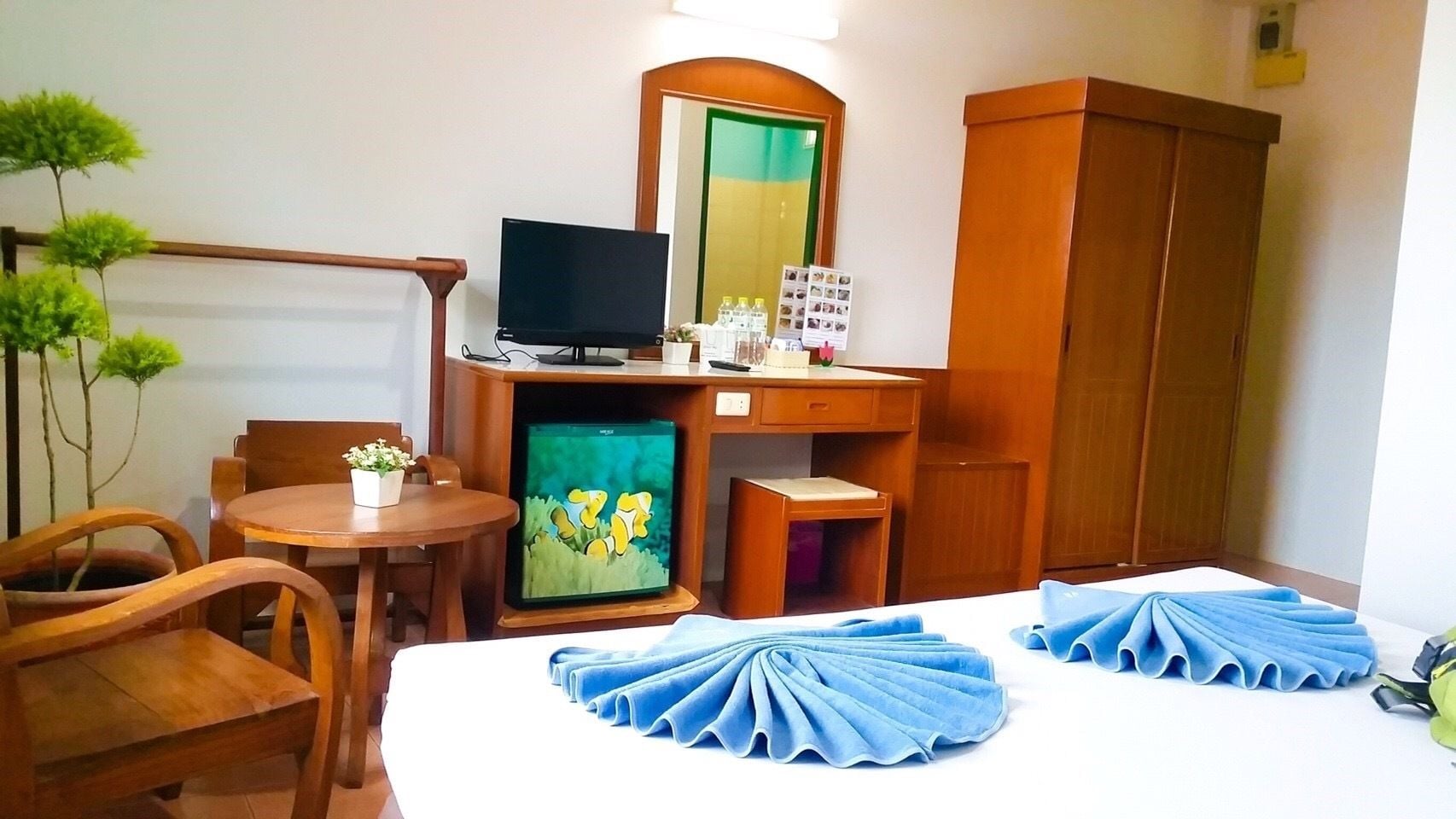 A hotel room with a bed, a desk with a computer, a chair, a small table, and a wardrobe.