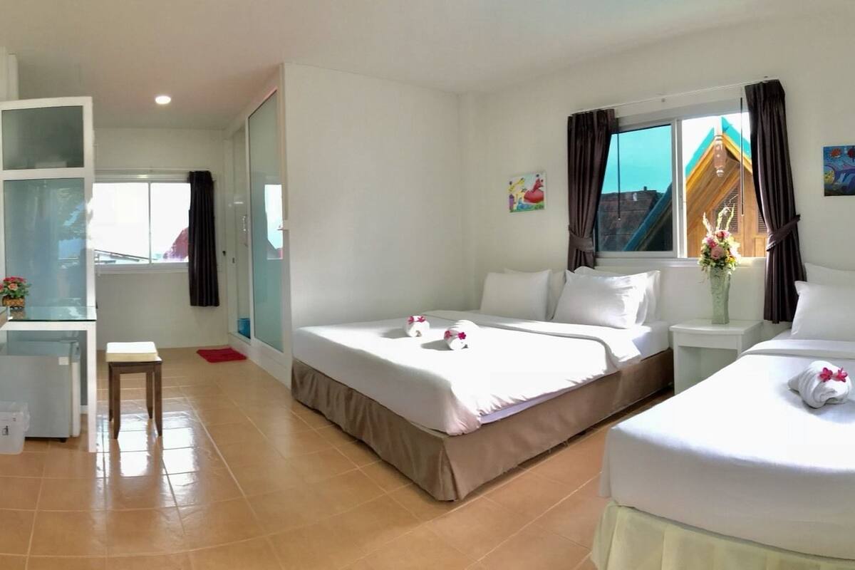 A hotel room with two beds, a desk, a TV, and a window with curtains.