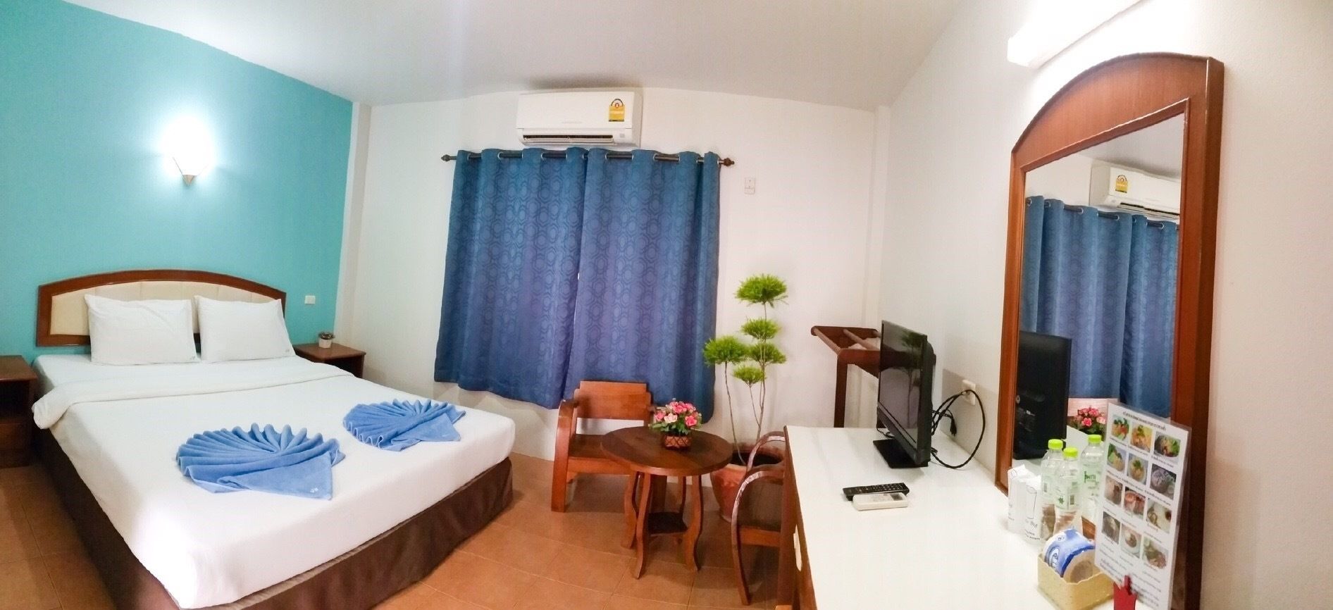 Habitación de hotel con cama, escritorio, silla, televisor y espejo.