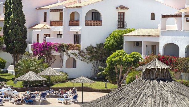 Un resort con piscina, poltrone a sdraio e ombrelloni di paglia.