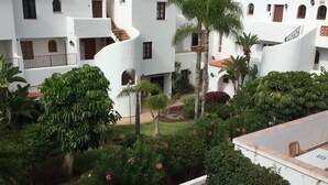 Un cortile con edifici bianchi, palme e un piccolo giardino con fiori rosa.