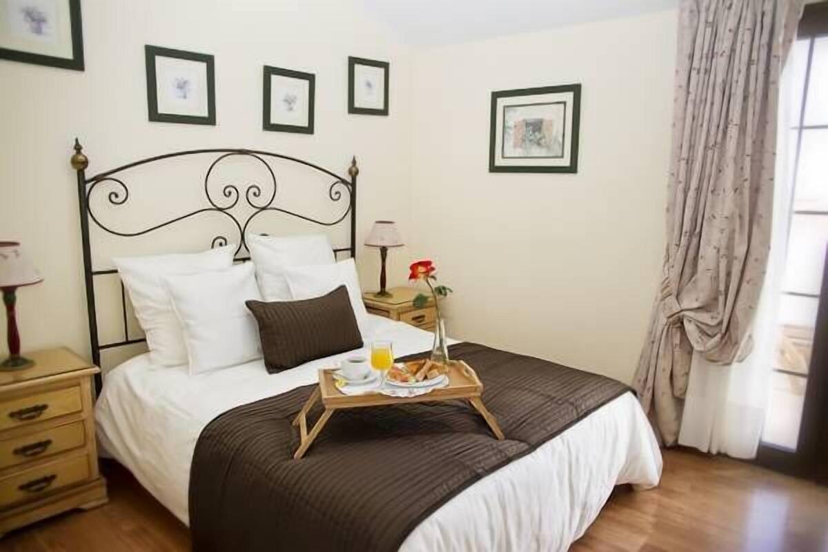 Een netjes opgemaakt bed met een tray ontbijt, een nachtkastje met een lamp, en ingelijste foto's aan de muur.
