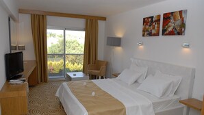 Hotellihuone, jossa on sänky, työpöytä, jossa on televisio, tuoli, lamppu ja näkymä vihreälle alueelle.