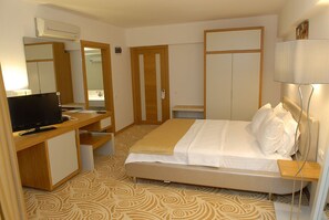 A hotel room with a bed, a desk with a computer, a mirror, and a wardrobe. - Hotel Egge (Cesme)