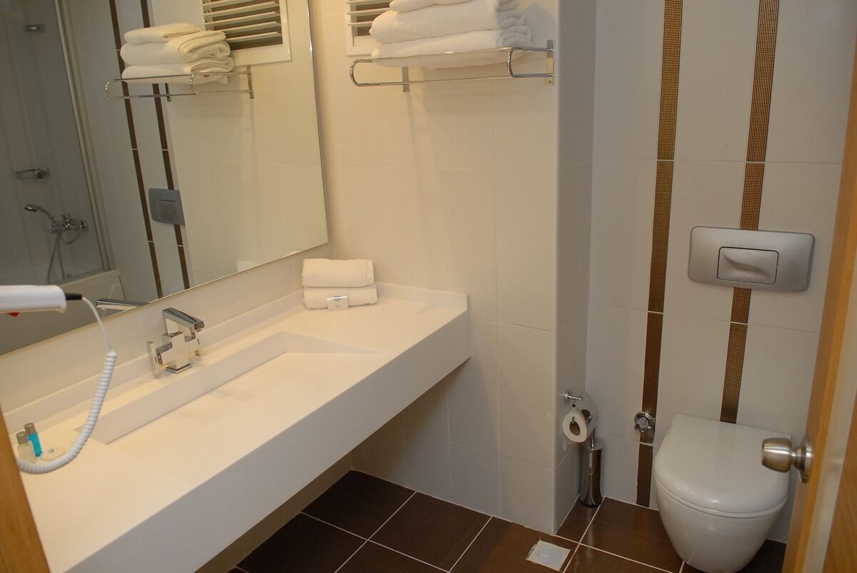 A bathroom with a white sink, a mirror, a toilet, and a shower area.