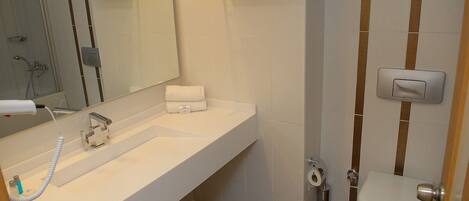 A bathroom with a white sink, a mirror, a toilet, and a shower area.