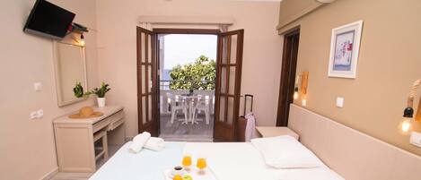 Habitación de hotel con cama, escritorio, silla, mesa con desayuno y balcón con vistas.