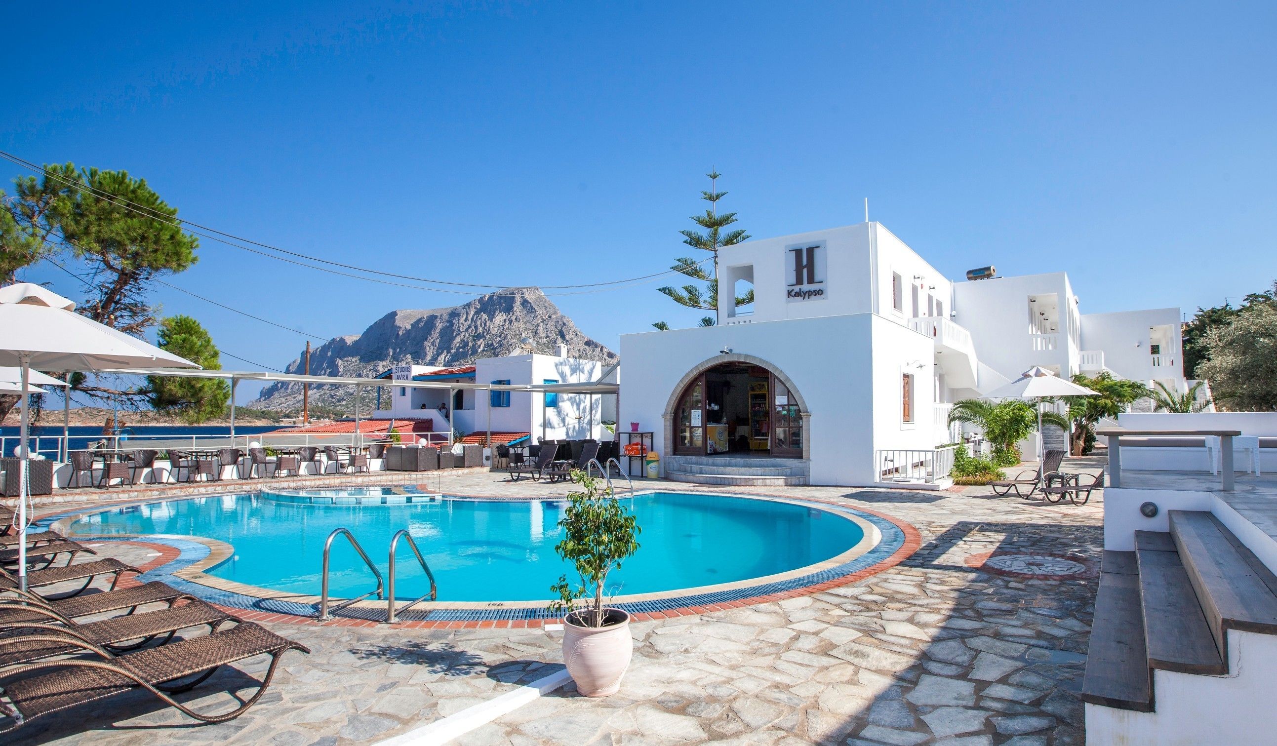 A pool area with lounge chairs, a potted plant, and a building with a sign reading "Kalypso".