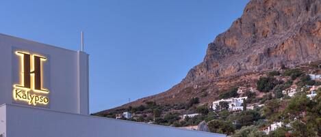 A hotel with a prominent illuminated sign, a modern architectural design, and a view of a mountainous landscape in the background.