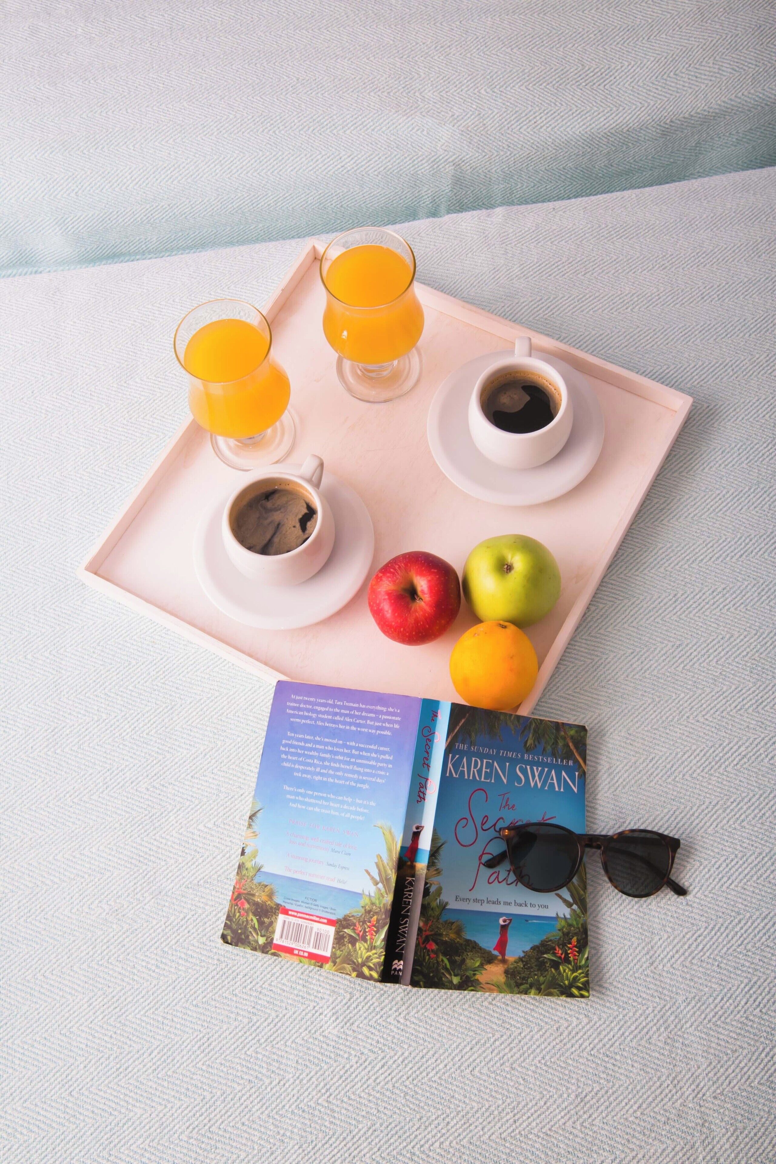 Een dienblad met een boek, zonnebril en ontbijtartikelen, zoals sap, koffie en fruit.
