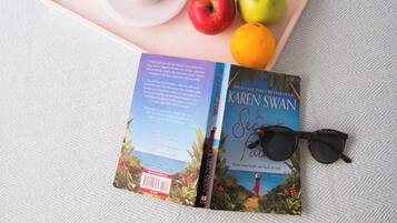 Una bandeja con un libro, gafas de sol y productos para el desayuno, como jugo, café y fruta.