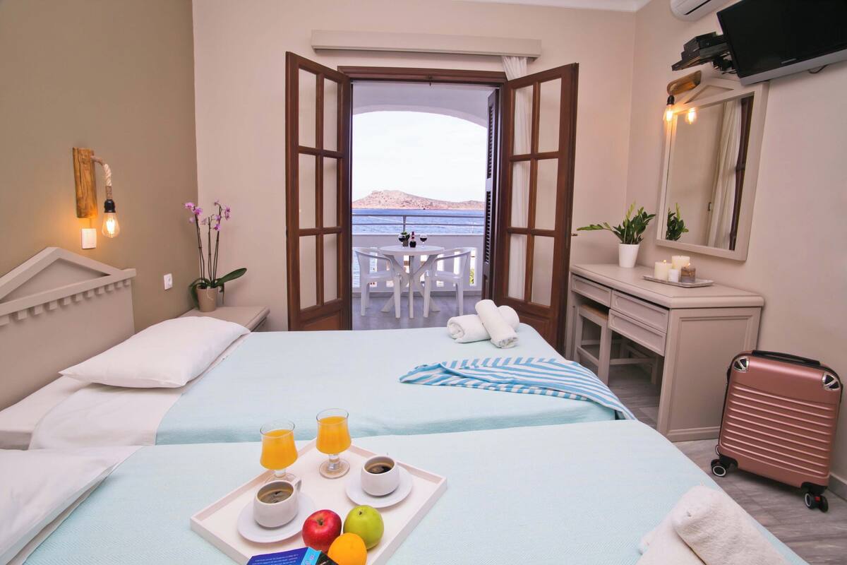A hotel room with a bed, breakfast tray, open balcony, and a desk with a mirror.