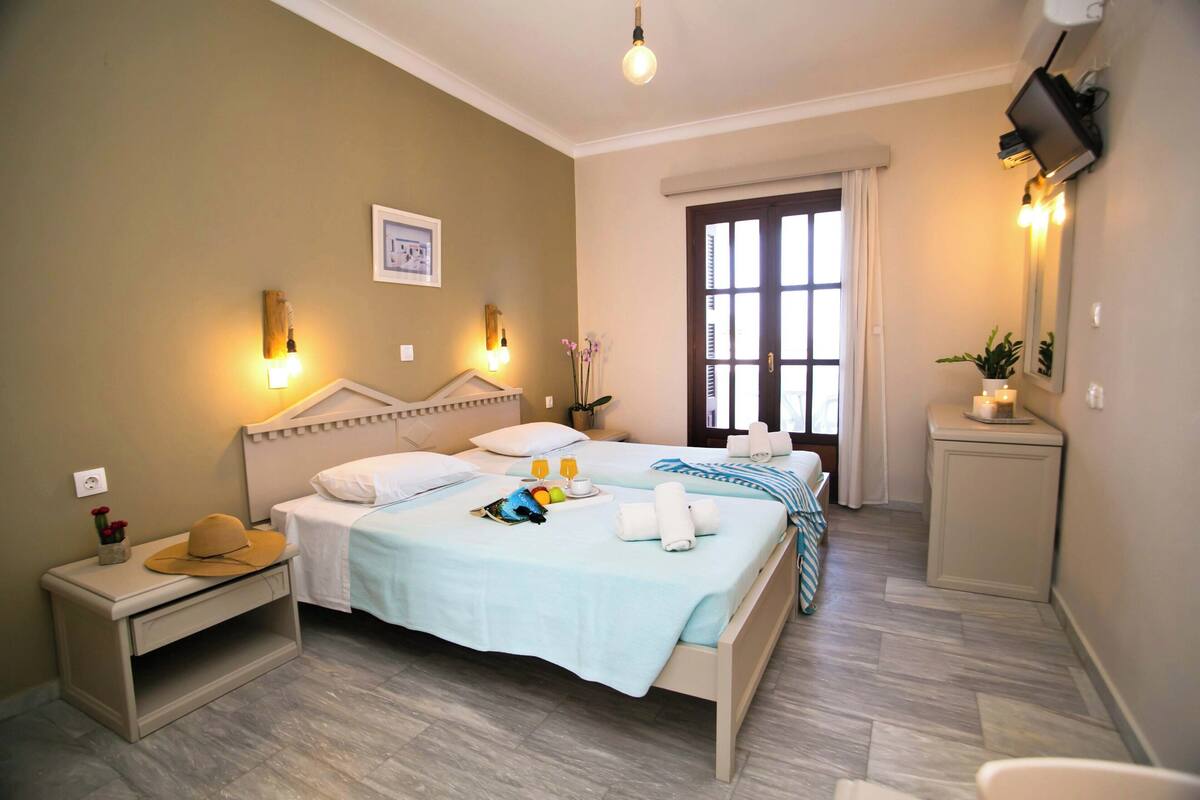 A hotel room with a bed, bedside table, lamp, and a window with curtains.
