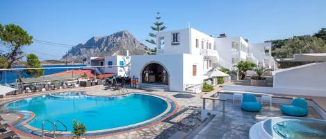 A swimming pool with a stone deck, lounge chairs, and a hot tub.