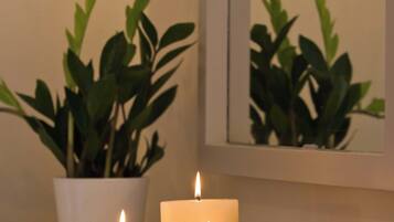 Escena iluminada por velas con dos velas sobre una bandeja, una planta en maceta y un espejo que refleja la planta.