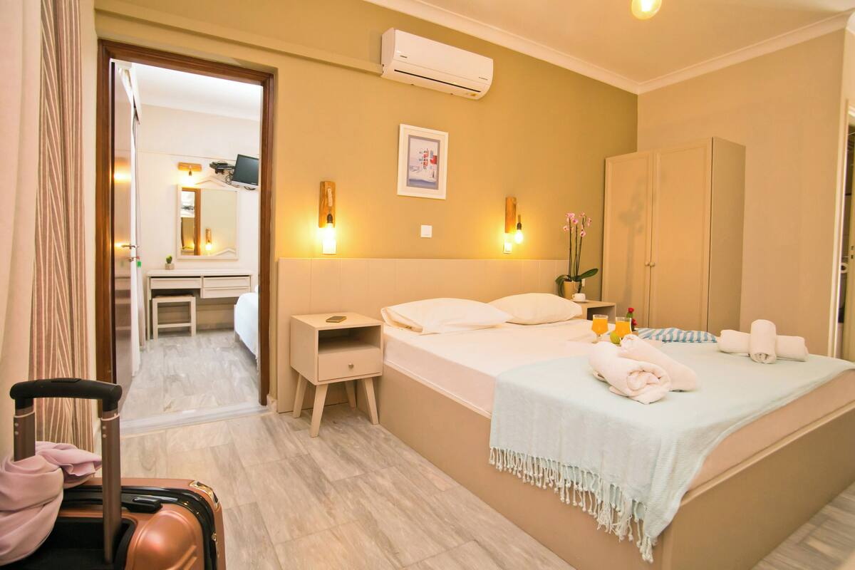 A hotel room with a bed, bedside table, nightstand, and a suitcase.
