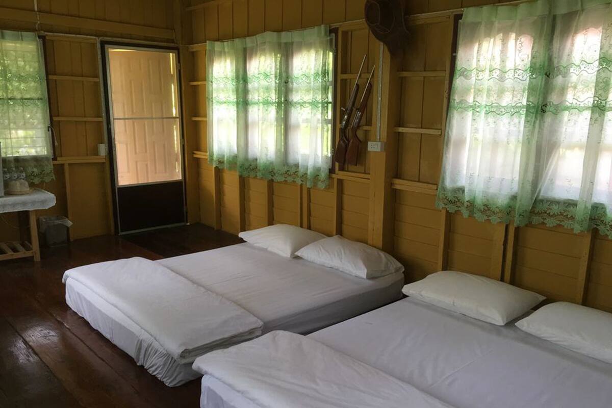 A room with three single beds, wooden walls, and a small desk with a chair.