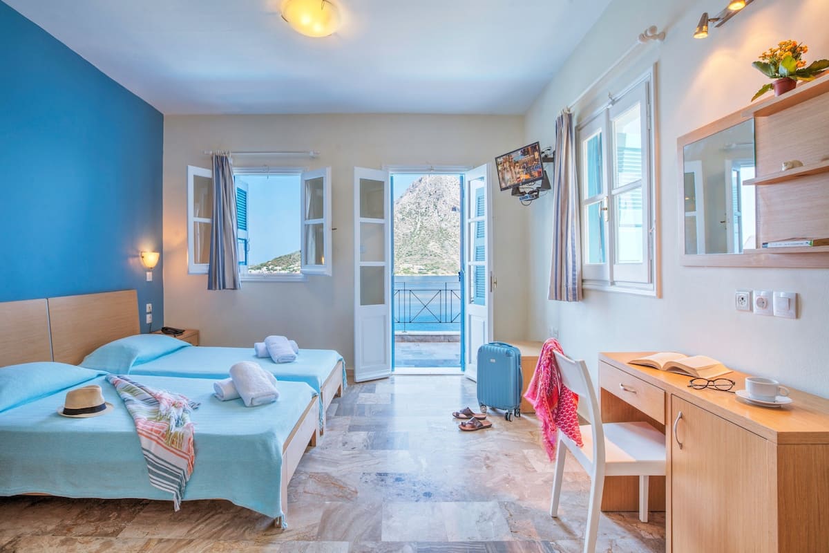 Habitación de hotel con dos camas, un escritorio, una silla, una maleta y vistas al exterior.