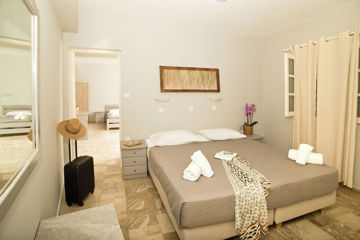 Habitación de hotel ordenada con una cama, una maleta, un sombrero y un espejo.