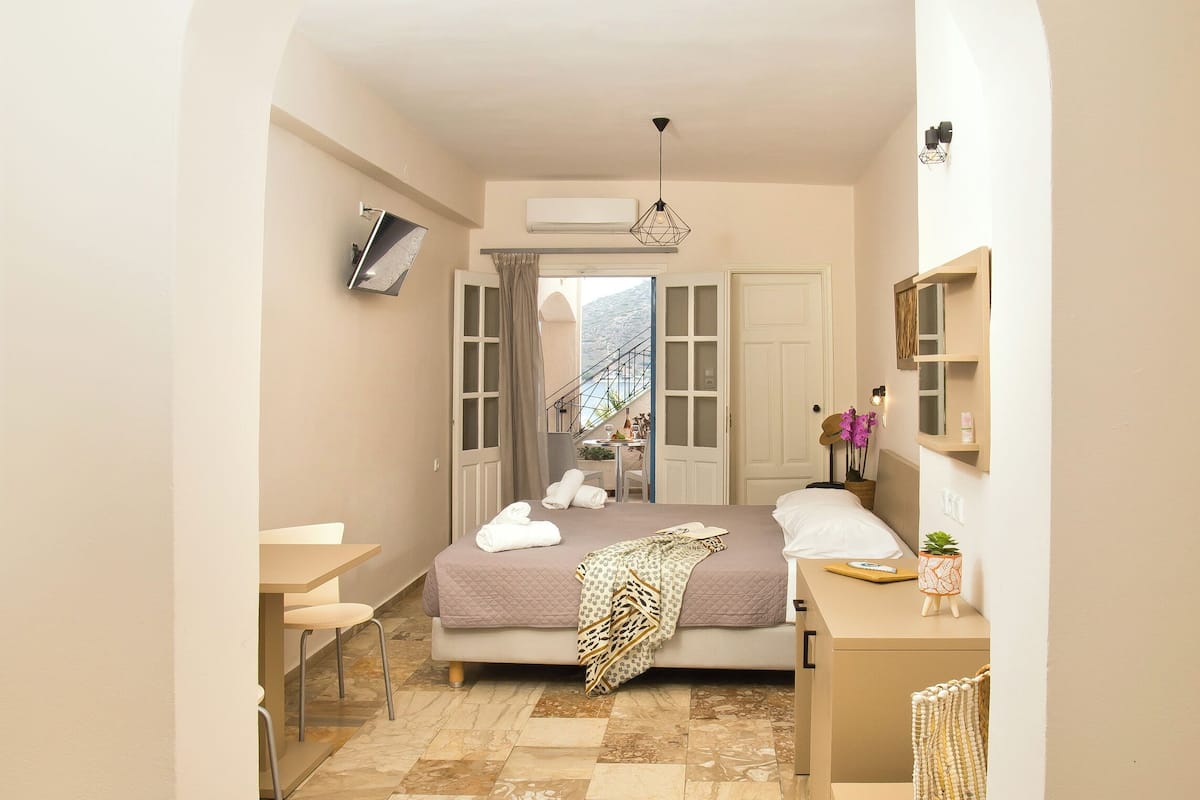 Un dormitorio con cama, mesitas de noche, escritorio, silla y baño con lavabo y espejo.