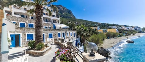 Un edificio costero con paredes de piedra, contraventanas azules y una palmera.