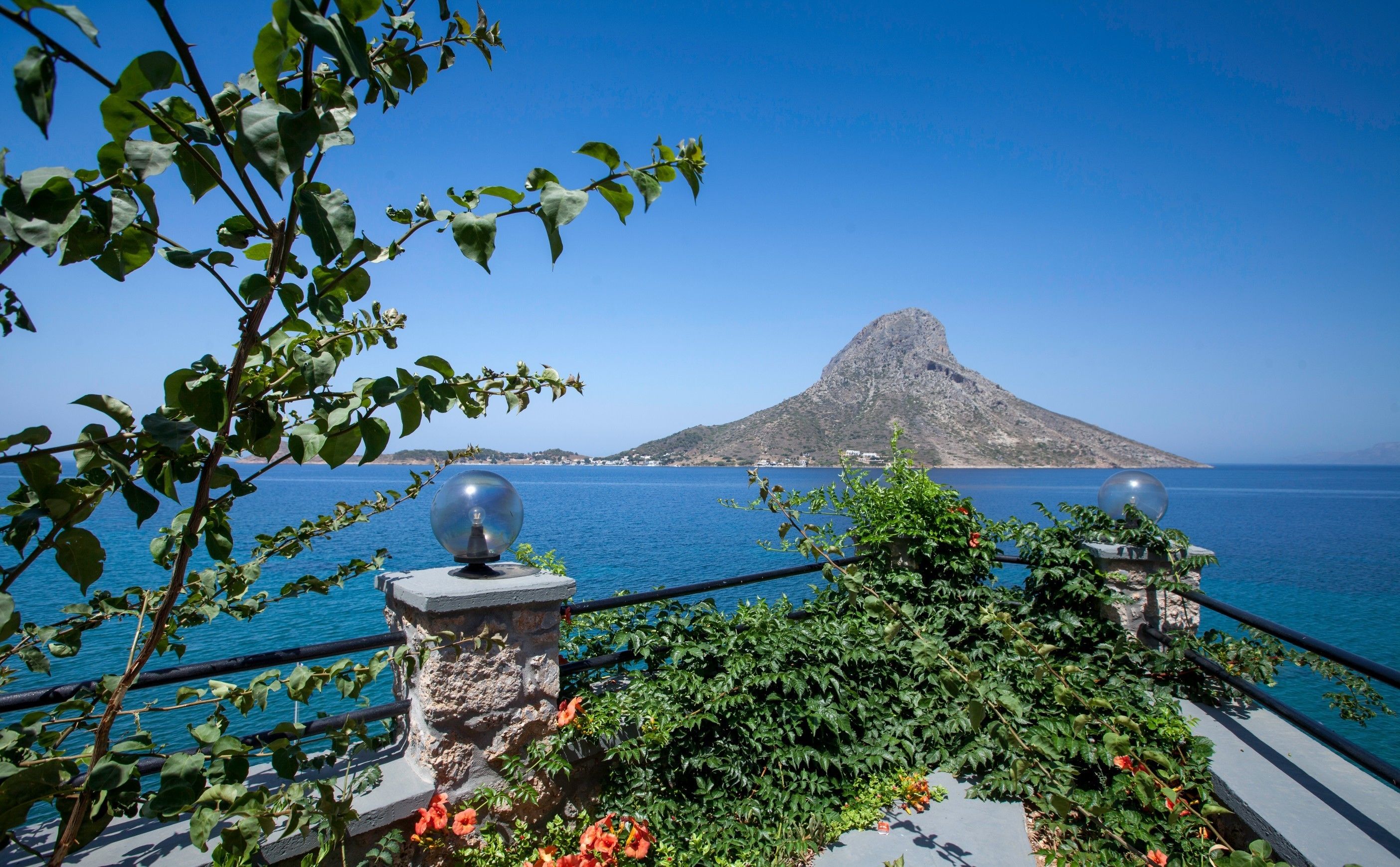 Blick auf die Küste mit einem markanten Berg, einem Geländer mit Kugelornamenten und üppiger Vegetation.