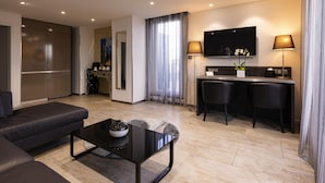 A modern hotel room with a sofa, a dining table with chairs, a TV, and a desk with lamps.