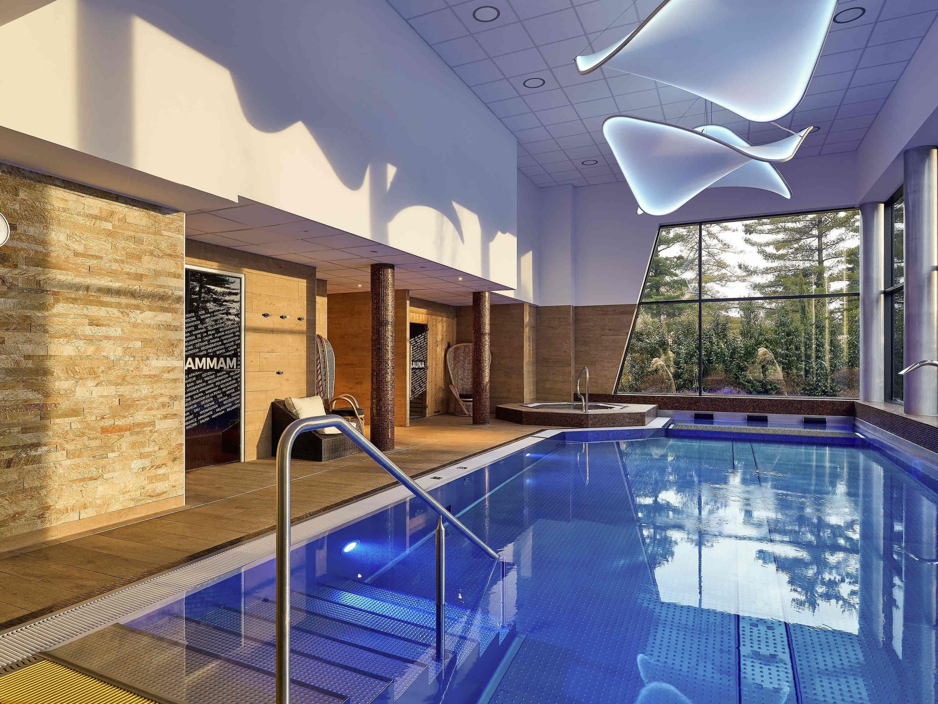Un área de piscina interior moderna con una barrera de vidrio transparente, una sala de sauna y vistas al exterior.