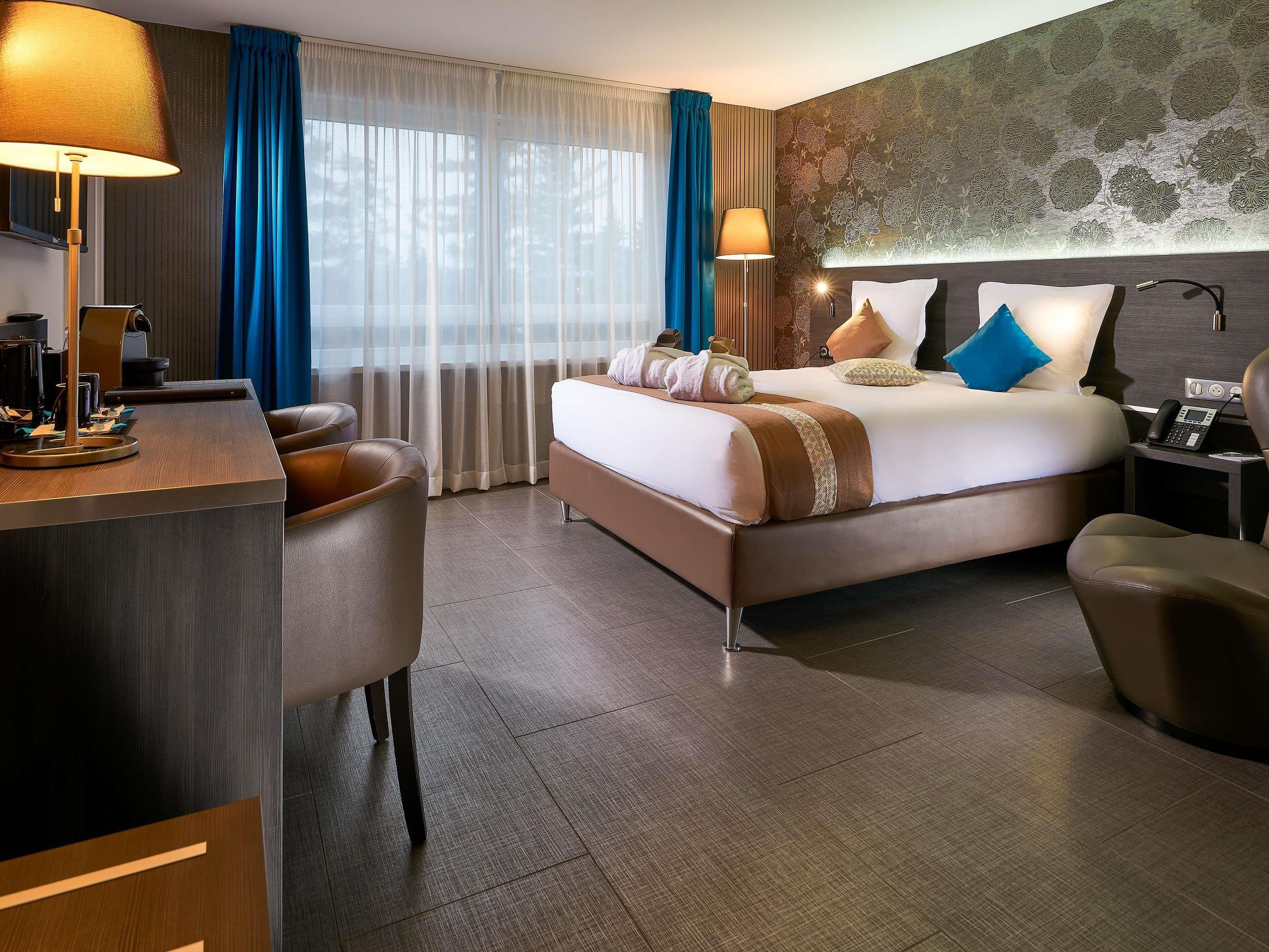 A hotel room with a bed, desk, chairs, and a nightstand with a phone.